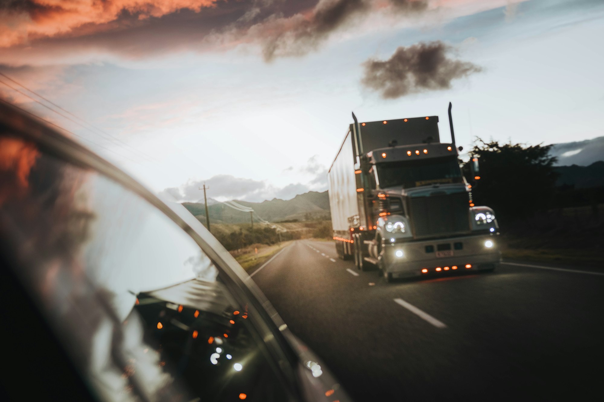 Semi truck with an enclosed trailer driving on an open highway at dusk